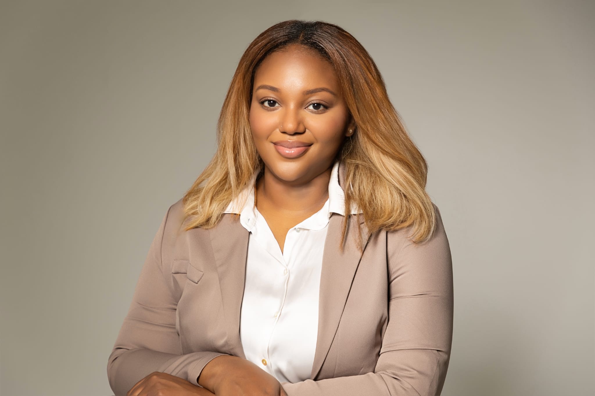 Une femme afro-américaine aux cheveux châtains vêtue d'un veston crème et d'une chemise blanche.